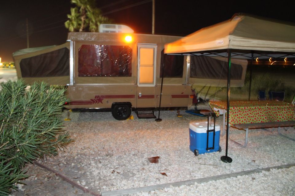 Pop-up camper with awning and cooler at campsite