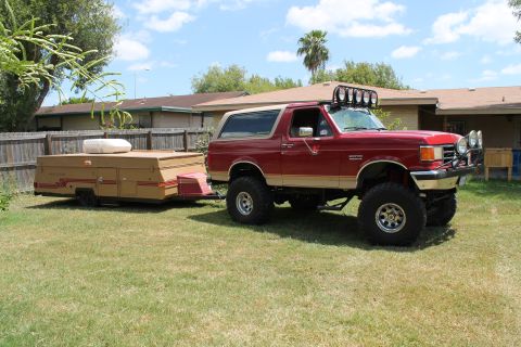 1990 Ford Bronco - Red 1990 Ford Bronco with a pop-up camper in tow, parked on a grassy lawn.