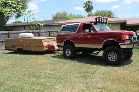 1990 Ford Bronco - A lifted 1990 Ford Bronco is parked on a lawn, hitched to a pop-up camper.