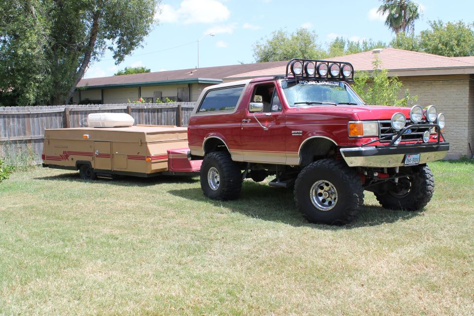 Red Ford Bronco with tan trim, lifted with large tires, towing a tan pop-up camper