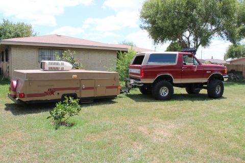 1990 Ford Bronco - A lifted 1990 Ford Bronco is parked in a grassy yard, hitched to a pop-up camper.