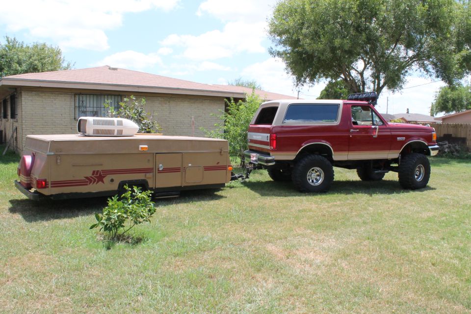 Red and tan lifted 1990 Ford Bronco towing a pop-up camper