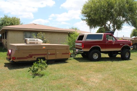 1990 Ford Bronco - Lifted 1990 Ford Bronco is seen towing a pop-up camper in front of a house.