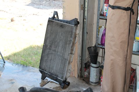 1990 Ford Bronco - A detached radiator rests on a concrete floor near a garage door, with shelves of supplies in the background.