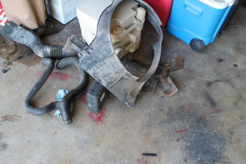1990 Ford Bronco - Assorted engine parts including hoses and a fan shroud are laid out on the floor next to a cooler.