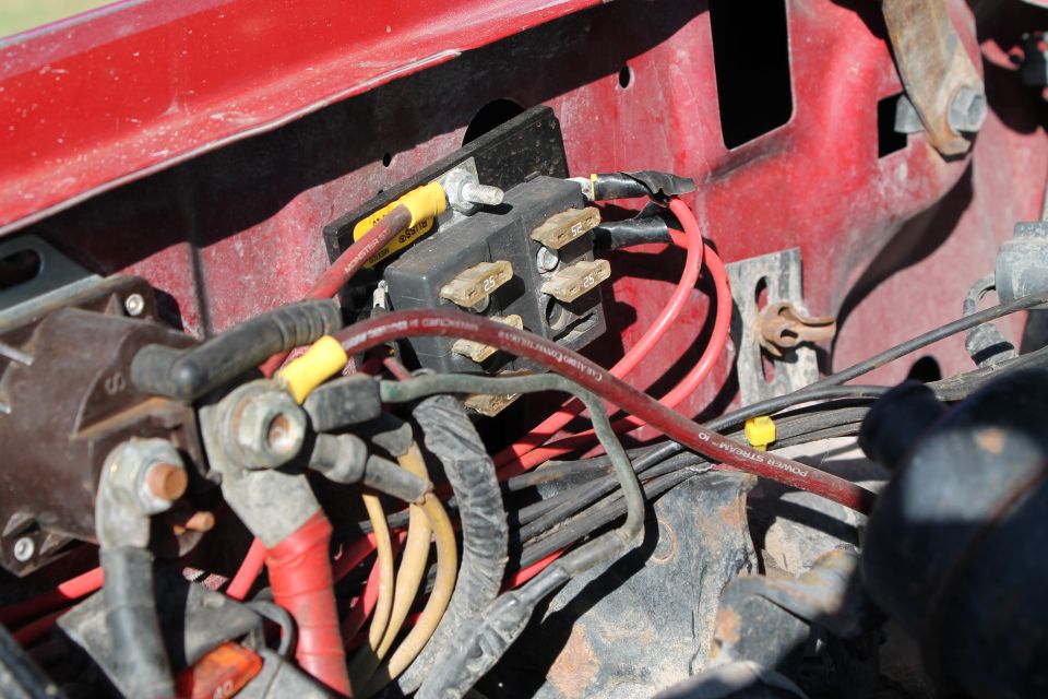 Close-up of a vehicle's engine bay wiring harness and fuse box with red and yellow wires