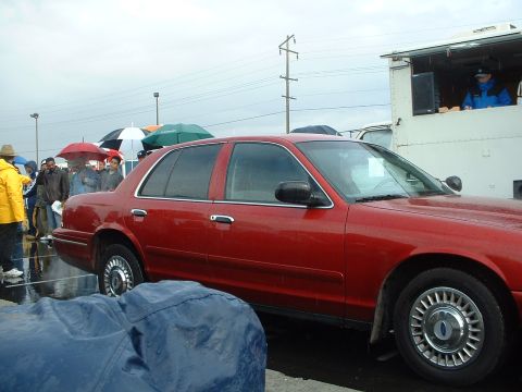 1999 Ford Crown Victoria - A red sedan is seen from the side in rainy weather, with people holding umbrellas in the background.