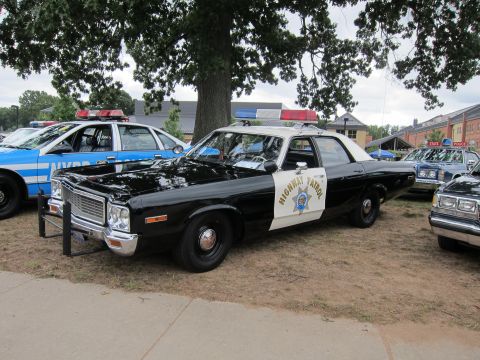 1991 Ford LTD Crown Victoria - black-and-white Highway Patrol sedan with a chrome grille, push bar and star door shield parked among other vintage police cars on grass.