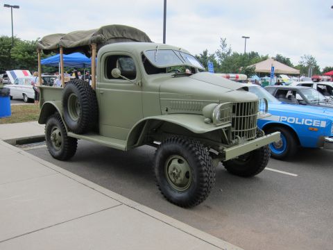 1991 Ford LTD Crown Victoria - olive-drab vintage Dodge military 4x4 pickup with canvas bed rack parks near a blue police car at a car show.
