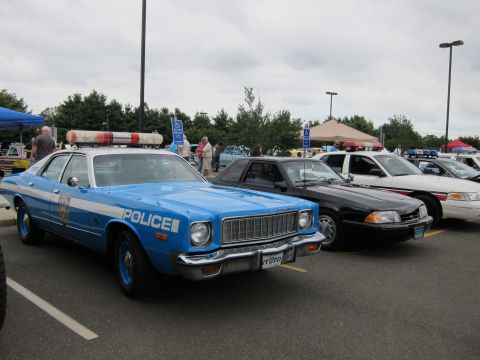 1991 Ford LTD Crown Victoria - light blue Plymouth police sedan lettered POLICE with a roof light bar sits among classic cars in a parking lot.