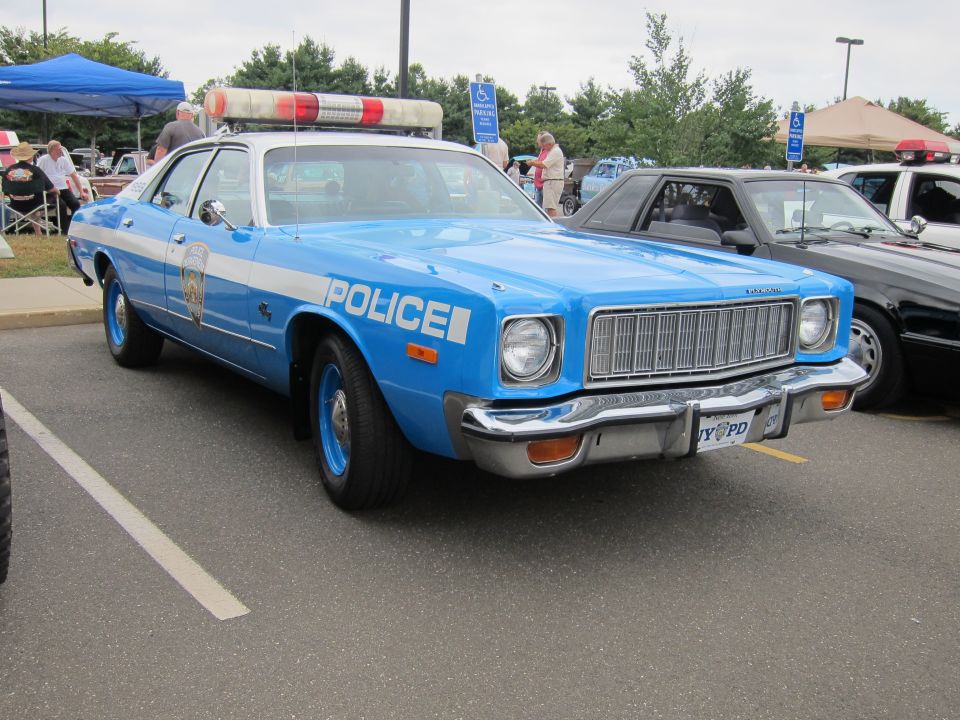 Light blue Plymouth police sedan with red roof light bar at a car show