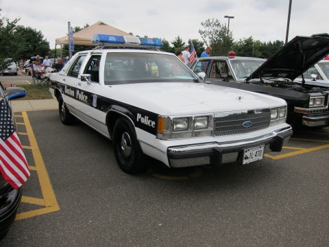 1991 Ford LTD Crown Victoria - black-and-white Ford LTD Crown Victoria lettered Boston Police with roof light bar sits beside a U.S. flag at a show.