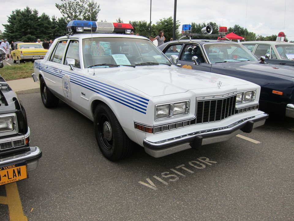White police sedan with blue stripes and roof light bar at an outdoor car show