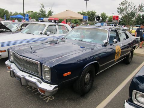 1991 Ford LTD Crown Victoria - dark blue Plymouth state-police sedan with chrome grille, roof light bar and speaker parks among cruisers at a car show.