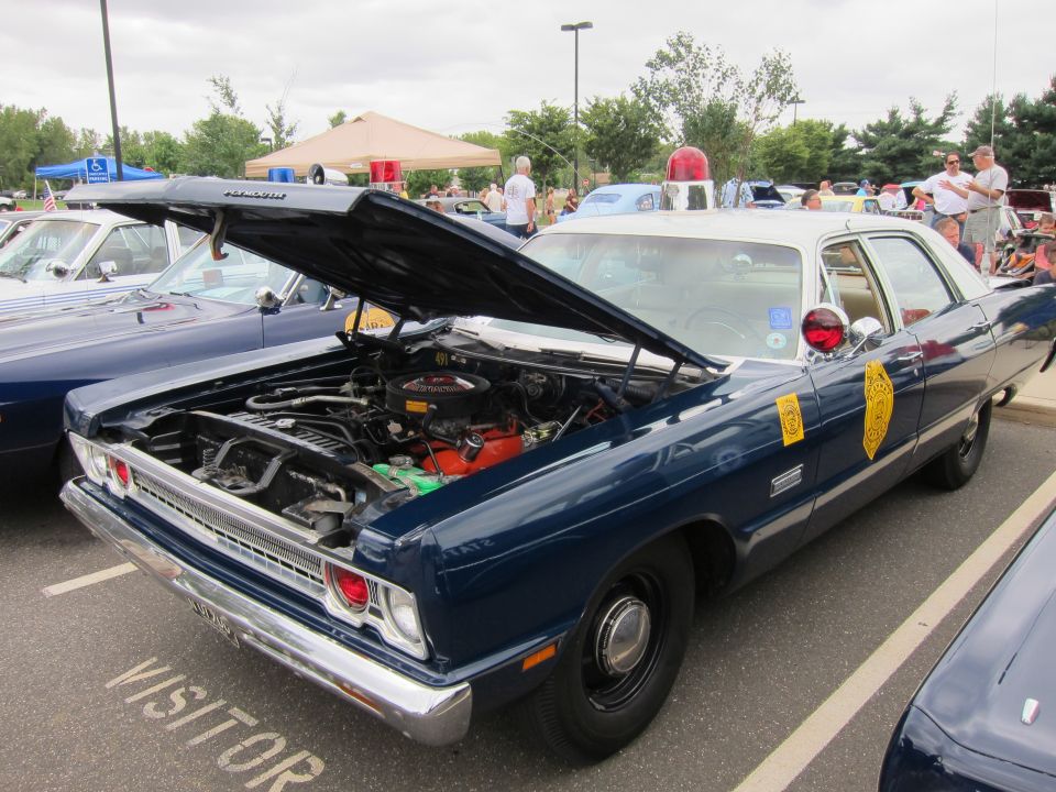 Dark blue state police sedan with hood open and gold door shield at a car show