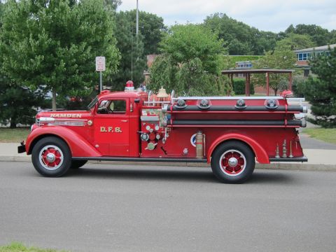 1991 Ford LTD Crown Victoria - Side view of a red vintage Hamden D.F.S. fire engine pumper truck with chrome details parked along a curb by trees.