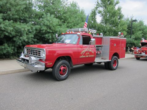 1991 Ford LTD Crown Victoria - Front three-quarter view of a red Dodge 4x4 fire pumper lettered Central Fire Co. parked on a road near evergreen trees.