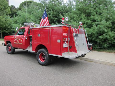 1991 Ford LTD Crown Victoria - Rear three-quarter view of a red forestry fire truck lettered Central Fire Co. with ladder rack and U.S. flag at a curb.
