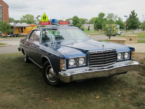 1991 Ford LTD Crown Victoria - blue vintage Ford state police sedan with a roof light bar parked on grass, with a school-crossing sign behind it.