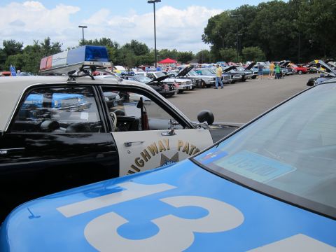 1991 Ford LTD Crown Victoria - Close-up of vintage police cars showing a Highway Patrol door decal and a blue numbered car, with show cars lined up behind.