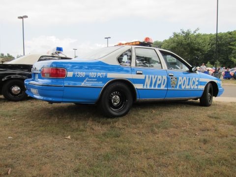 1991 Ford LTD Crown Victoria - blue NYPD police sedan marked 103 PCT with roof lights, rear three-quarter view, parked on grass at a car show.
