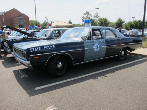 1991 Ford LTD Crown Victoria - blue-and-gray vintage state police sedan with door seal and roof lights parked on pavement among other show cars.