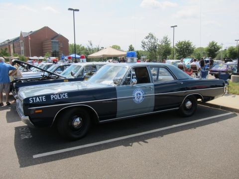 1991 Ford LTD Crown Victoria - dark-blue and gray vintage state police sedan with a roof light bar parked on pavement near a brick building.