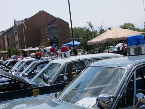 1991 Ford LTD Crown Victoria - tight row of vintage police cars seen along their roofs, topped with red and blue rotating light beacons, near a brick building.