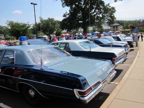 1991 Ford LTD Crown Victoria - Light-blue and dark-blue vintage state police sedans seen from the rear, parked in a row at a busy outdoor car show.