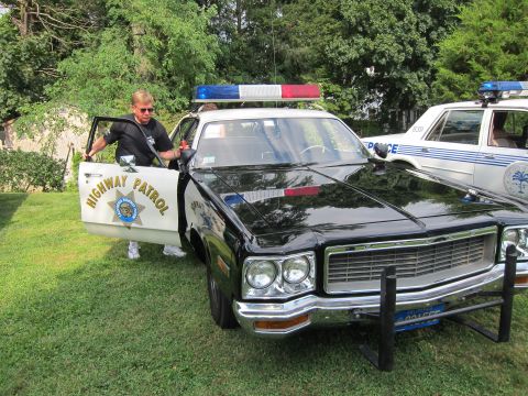 1991 Ford LTD Crown Victoria - man opens the door of a black-and-white Highway Patrol sedan with roof lights, parked on a lawn beside another cruiser.