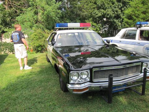 1991 Ford LTD Crown Victoria - man stands beside a black-and-white police sedan with roof light bar on a grassy lawn, another cruiser to the right.
