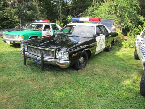1991 Ford LTD Crown Victoria - black-and-white highway patrol police sedan with chrome pushbar and roof light bar parked on grass beside other vintage cruisers.