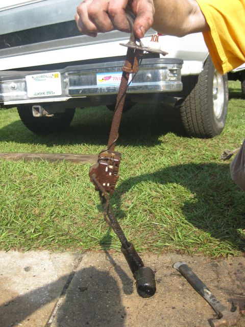 1994 Ford Bronco - A rusty metal lever is held up in front of the rear of a 1994 Ford Bronco.