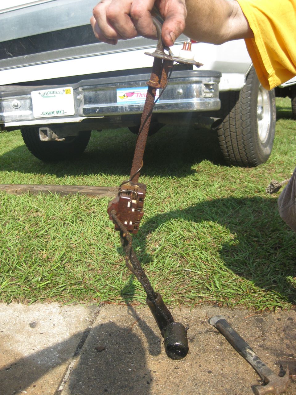 Rusty metal lever part held in front of a 1994 Ford Bronco's rear bumper and license plate