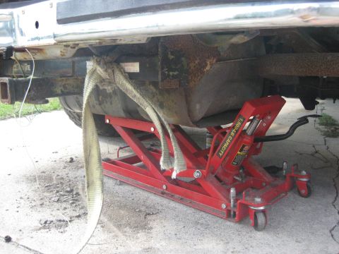 1994 Ford Bronco - A red hydraulic jack is positioned under the undercarriage of a vehicle, supporting its weight.