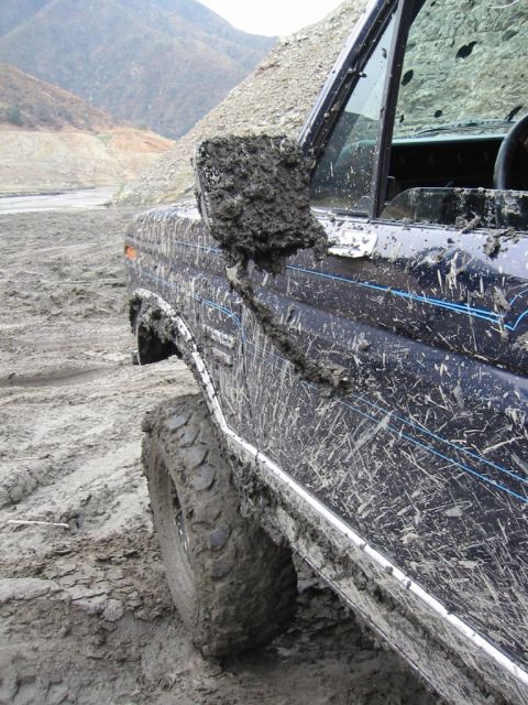 1985 Ford Bronco - This 1985 Ford Bronco is heavily covered in mud, showing its off-road capabilities.