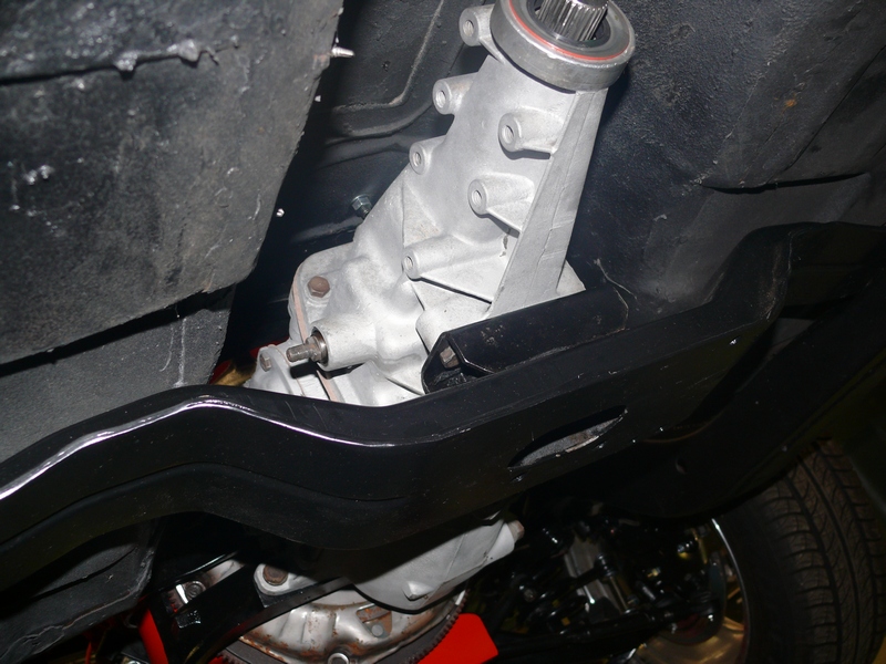 Underside view of a vehicle's transmission and frame, showing a silver gearbox and black metal components