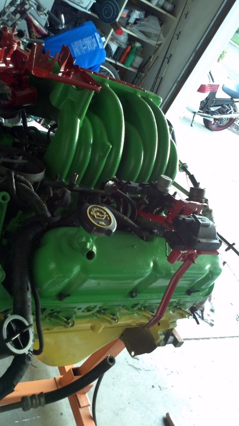 1987 Ford Bronco - Engine part on a stand, with green and red paint, in a garage setting.