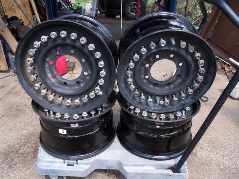 1989 Ford Bronco - Four black wheels with many lug nuts are stacked on a dolly in a workshop setting.