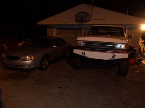 1989 Ford Bronco - Two vehicles, a white Ford F-Series truck and a silver Ford Taurus, are parked in a driveway at night.