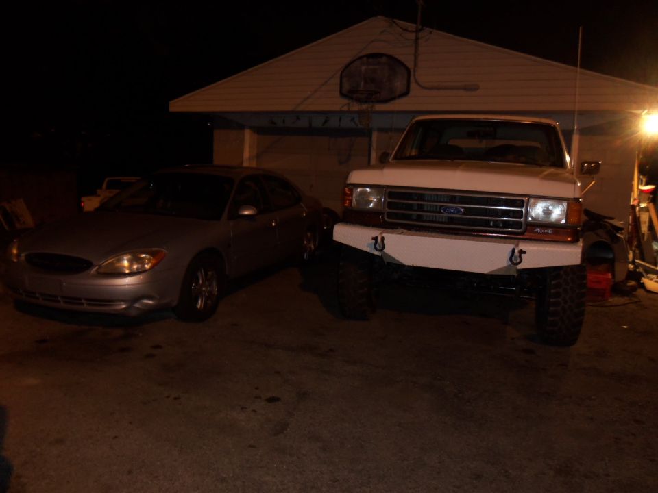White Ford F-Series truck with aftermarket bumper parked next to a silver Ford Taurus