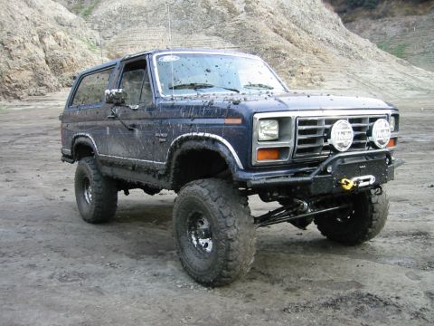1985 Ford Bronco - Mud-covered Ford Bronco parked on dirt with a rocky hill in the background.