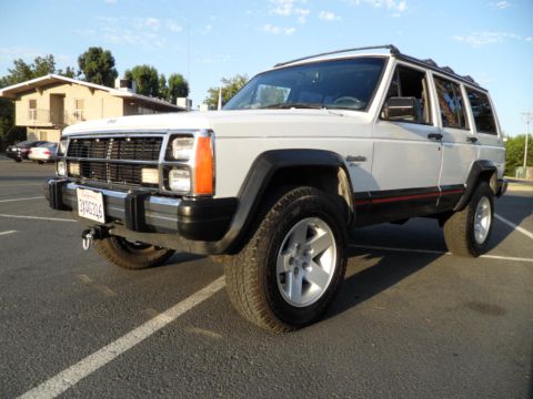 1994 Jeep Cherokee - White 1994 Jeep Cherokee with red and black side trim parked in a lot under a clear sky.