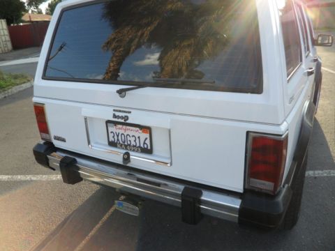 1994 Jeep Cherokee - The rear of a white Jeep Cherokee is shown, reflecting a palm tree in its window.