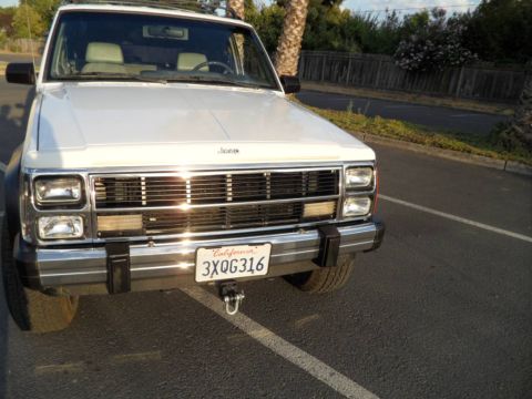 1994 Jeep Cherokee - A white Jeep Cherokee is parked on asphalt, showing its front grille and California license plate.