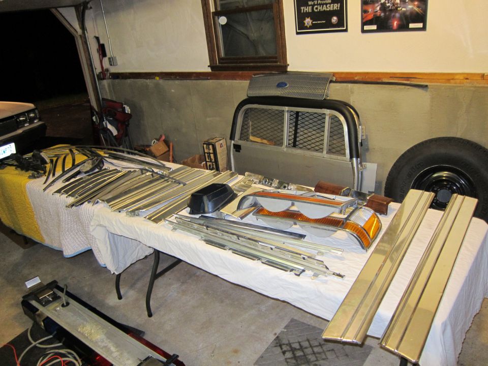 Car parts including trim, lights, and a grille laid out on tables in a garage