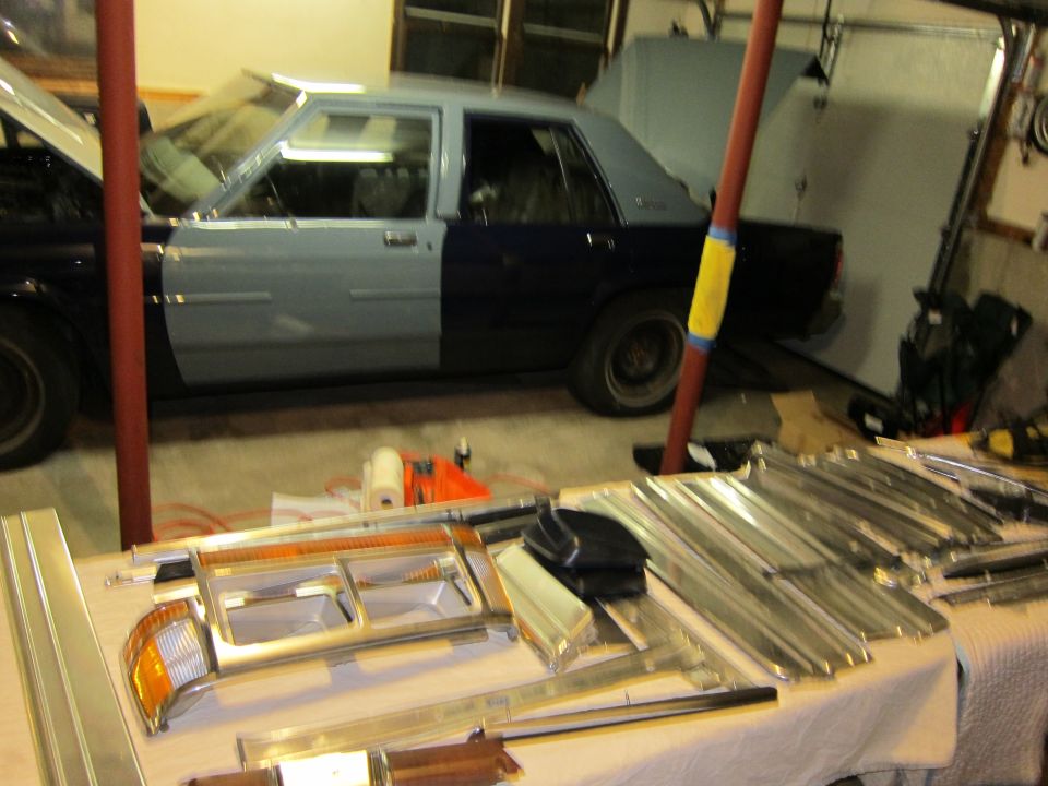 Side view of a two-tone sedan with hood and trunk open, parts laid out on a table