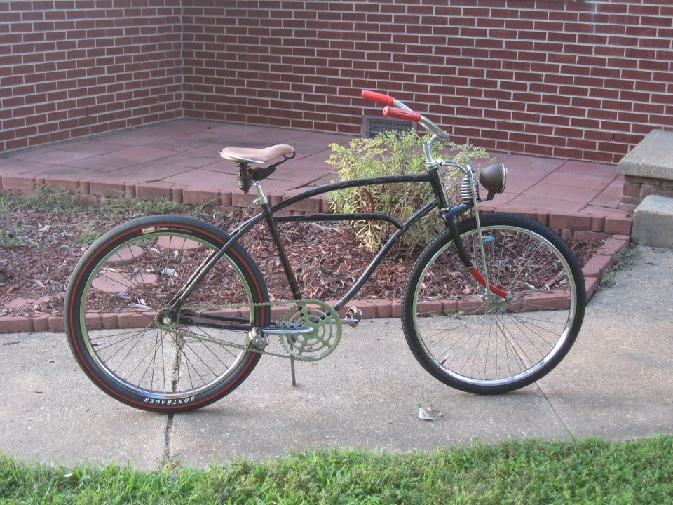 Black cruiser bicycle with red handlebars, tan seat, and a headlight