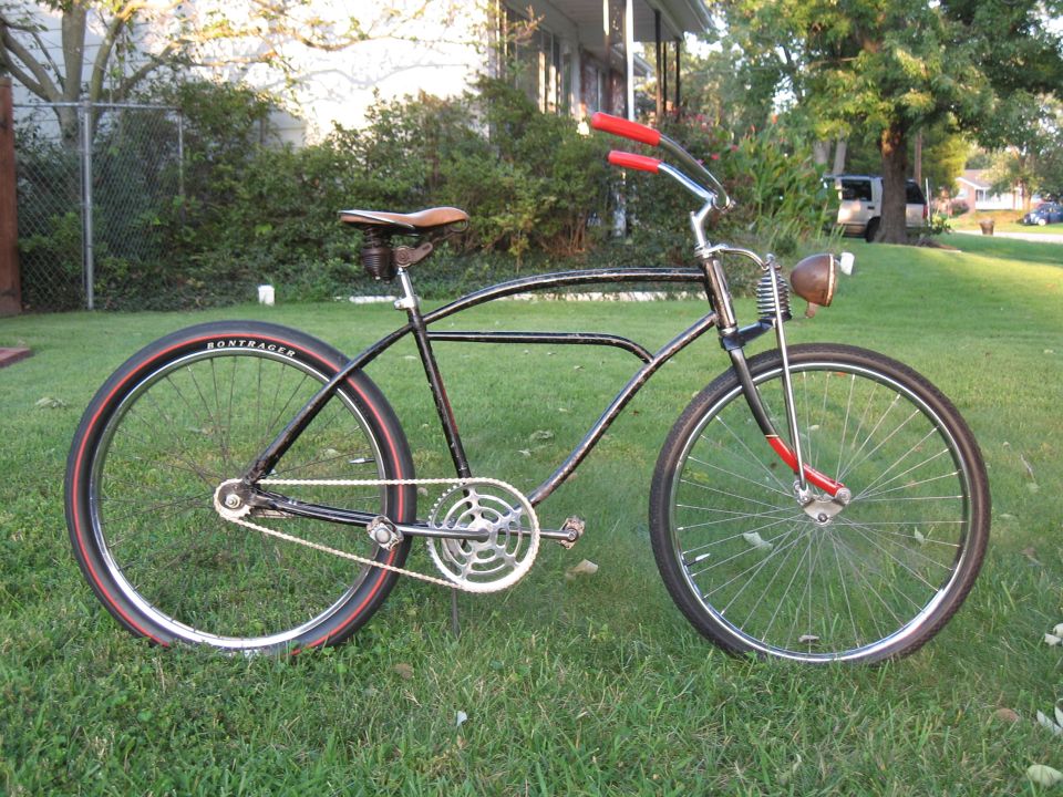 Black cruiser bicycle with red handlebars and seat, parked on grass