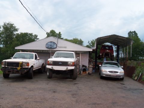 1989 Ford Bronco - Multiple vehicles are parked in a driveway, including two Ford trucks and a sedan, with another truck on a lift.